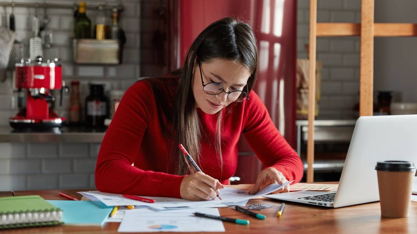 Mujer emprendedora mexicana anotando ventas en una libreta con billetes y monedas organizados.