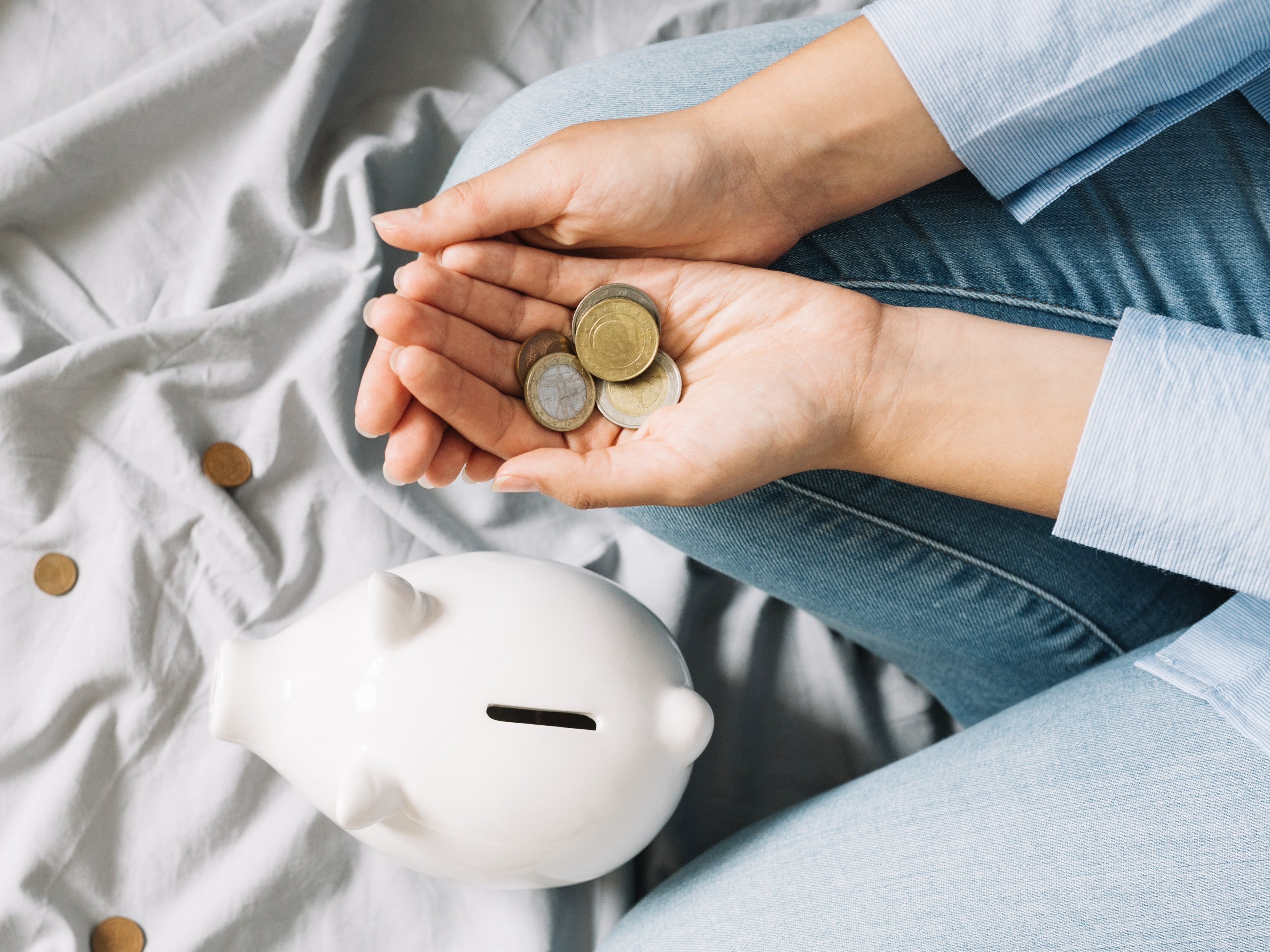 Mujer con monedas de peso mexicano, lista para meterlas en una alcancía para evitar los gastos hormiga y comenzar su ahorro.