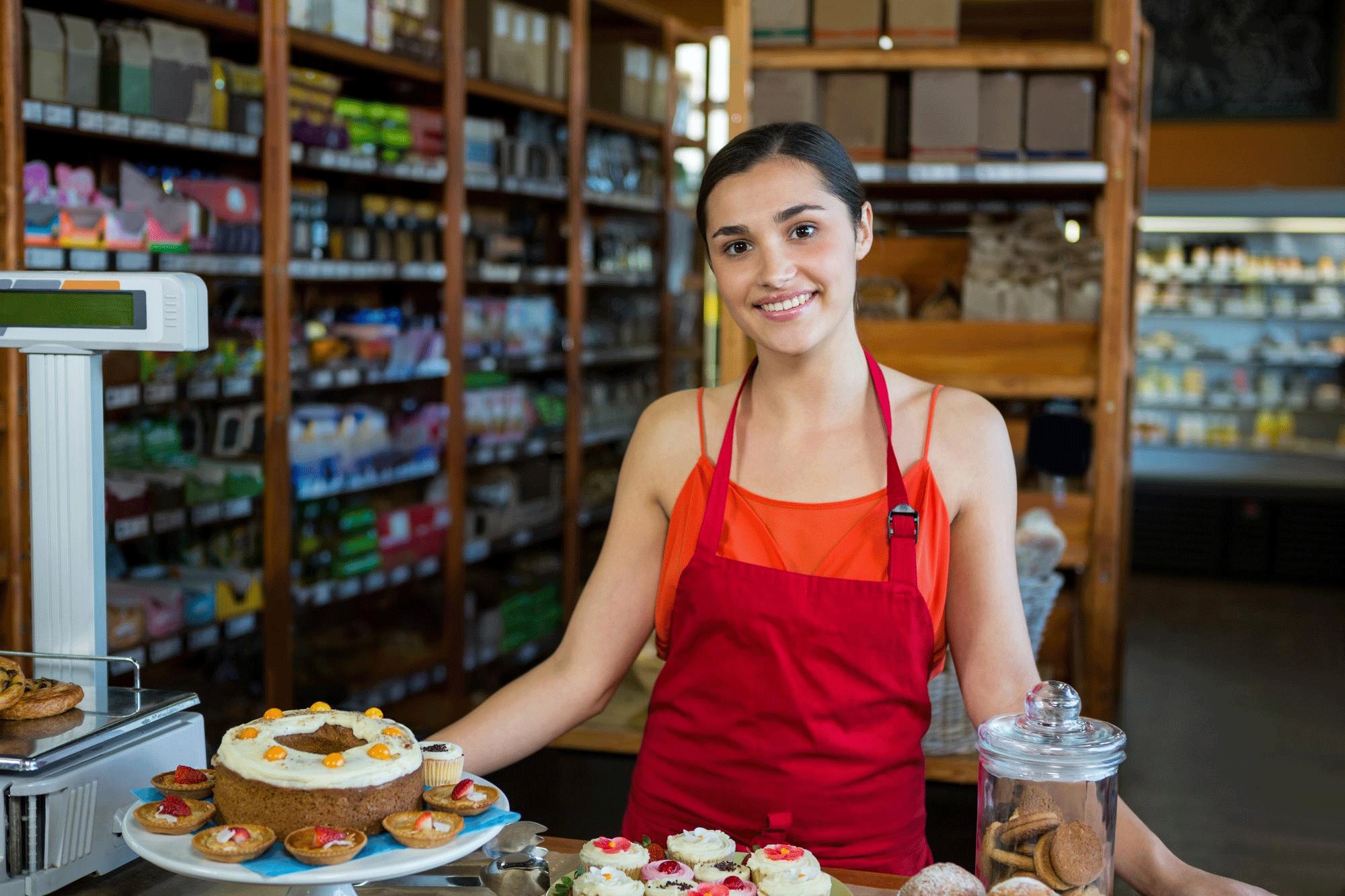 Comerciante sonriente en el mostrador de su local limpio, iluminado y decorado.
